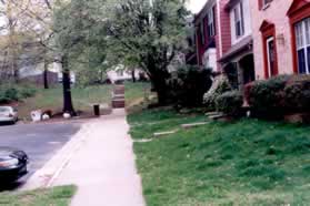 The sidewalk passes houses on the right and parking on the left.