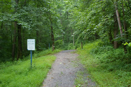 The trail crosses a water main. The trail surface changes to asphalt.