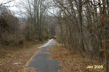 The trail leads through the woods on the way to a bridge.