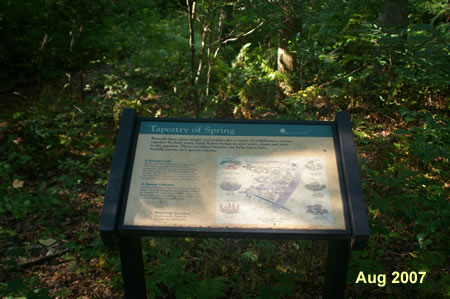 After walking to the back of the wildflower exhibit face this exhibit. Take the trail to the left that follows the stream downhill.en.  Turn left and follow the path marked by the arrow added to the picture.