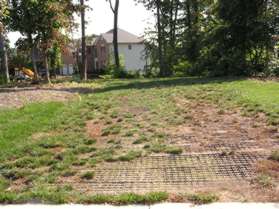 Turn left along the steel grate buried in the ground .  The grate is just prior to the house shown in the previous picture.