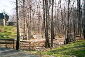 Path crosses bridge to left and turns right past tot lot shown.