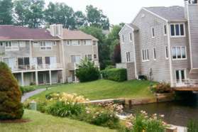 The trail goes down to the lake, turns left, and then right again between the houses.