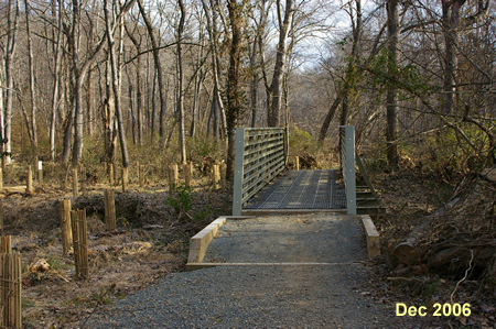 The trail crosses a short bridge over a ditch.