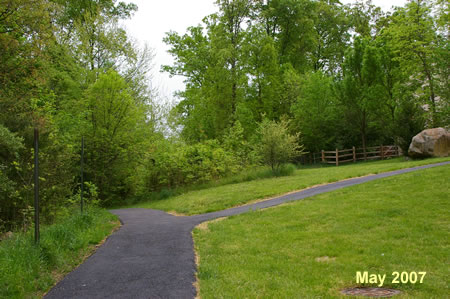 An asphalt trail intersects from the right. Continue straight on the present trail.