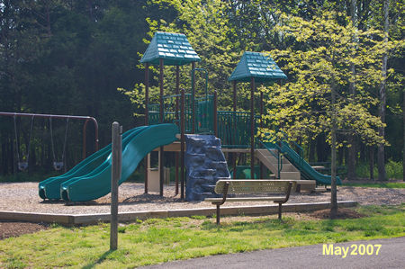 The play area has a large jungle gym, swings, and shaded picnic tables.